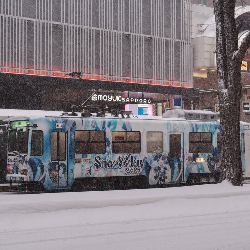 A picture of the Sapporo city tram in the seasonal Snow Miku wrap as it
passes the Moyuk Sapporo shopping mall on a snowy day.
